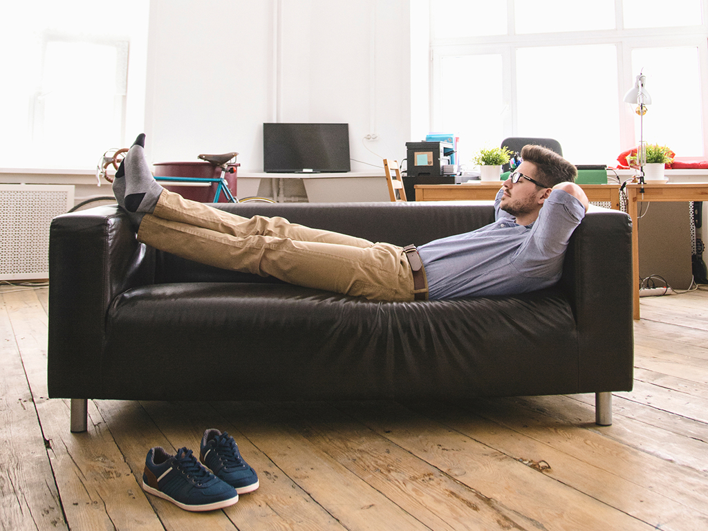 Tired businessman relaxing on sofa in light office room